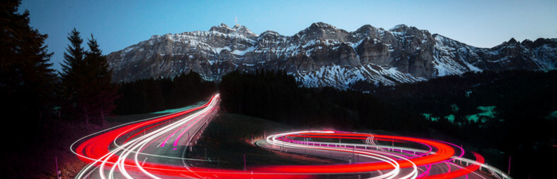 Kurvenreichen Straße, die durch die roten Rücklichter der Fahrzeuge beleuchtet wird, vor dem Hintergrund von Bergen.